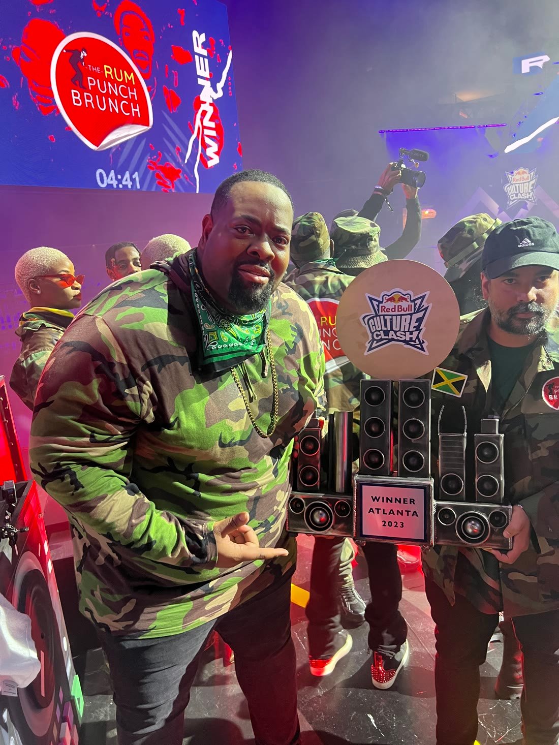 Prince Charm on stage holding the Red Bull Culture Clash trophy under the winner screen