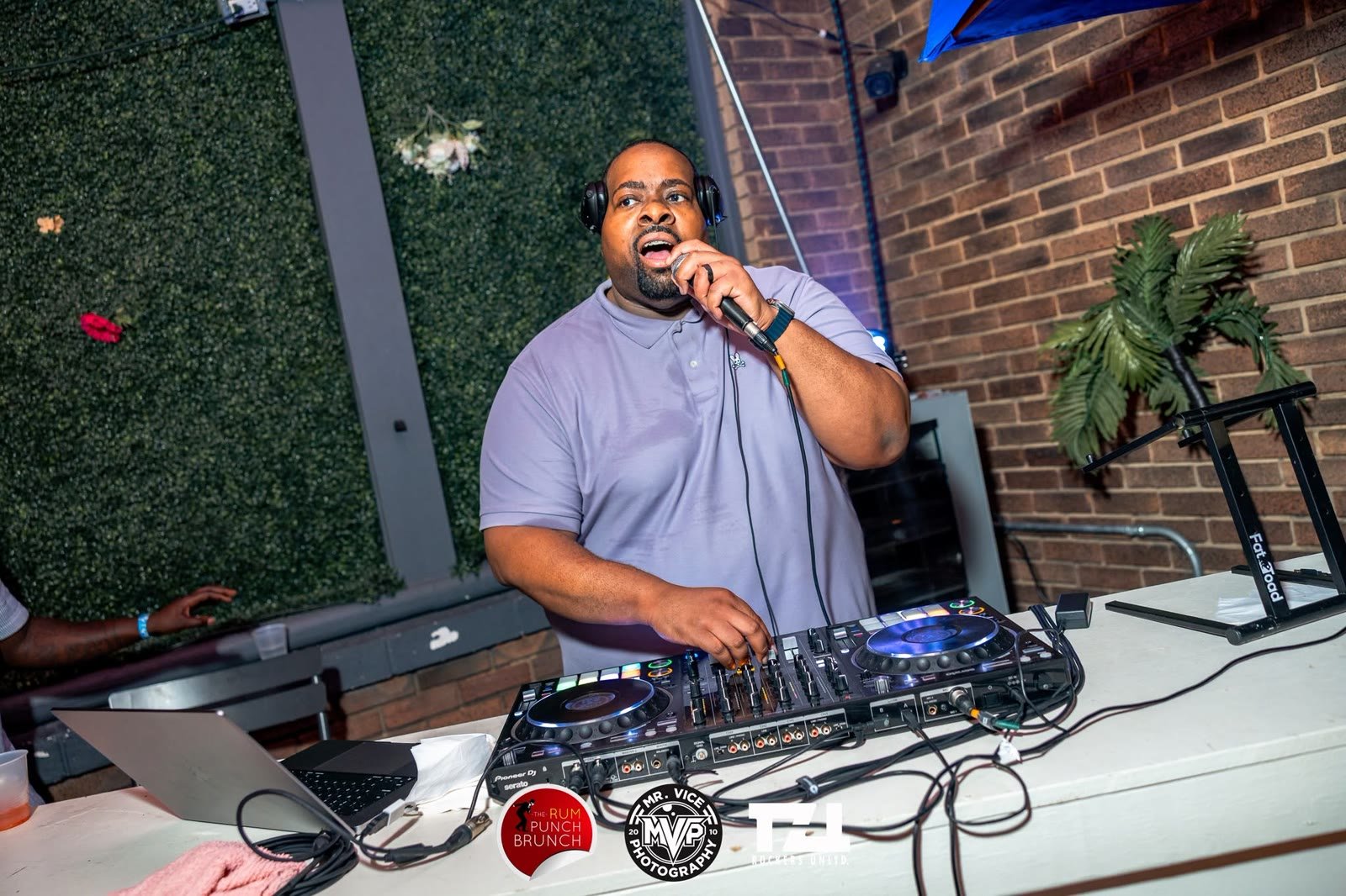 Prince Charm on the mic behind the decks at an outdoor brunch party